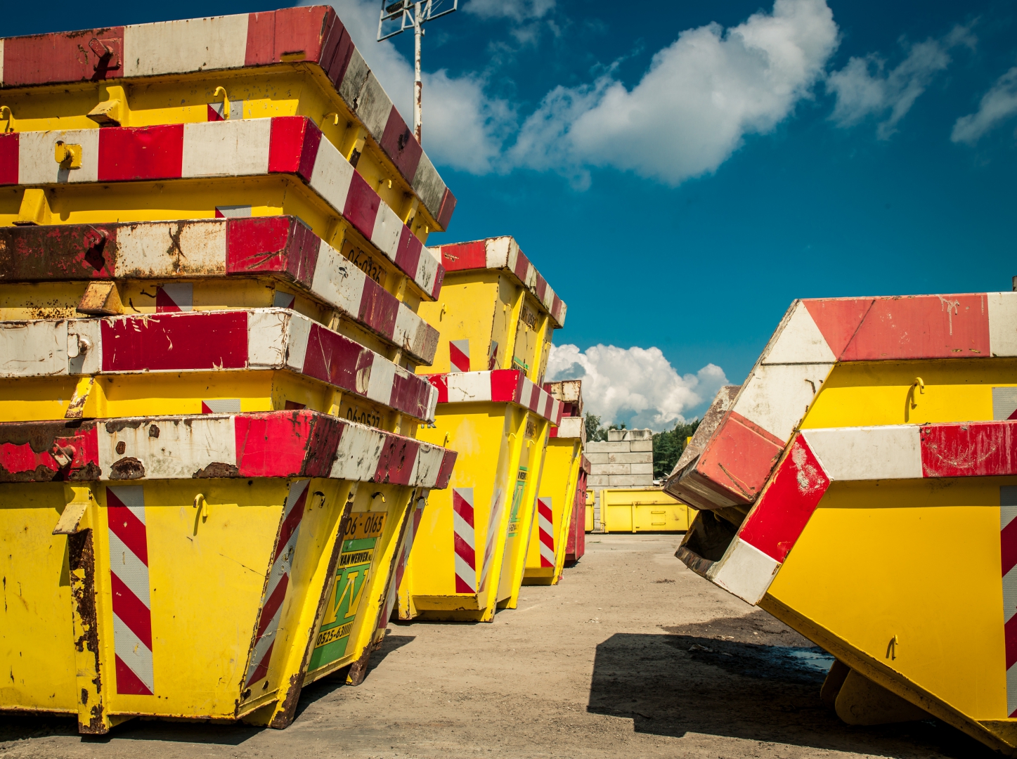 Gestapelde gele afzetcontainers met rood-witte markering van Van Werven onder een blauwe lucht