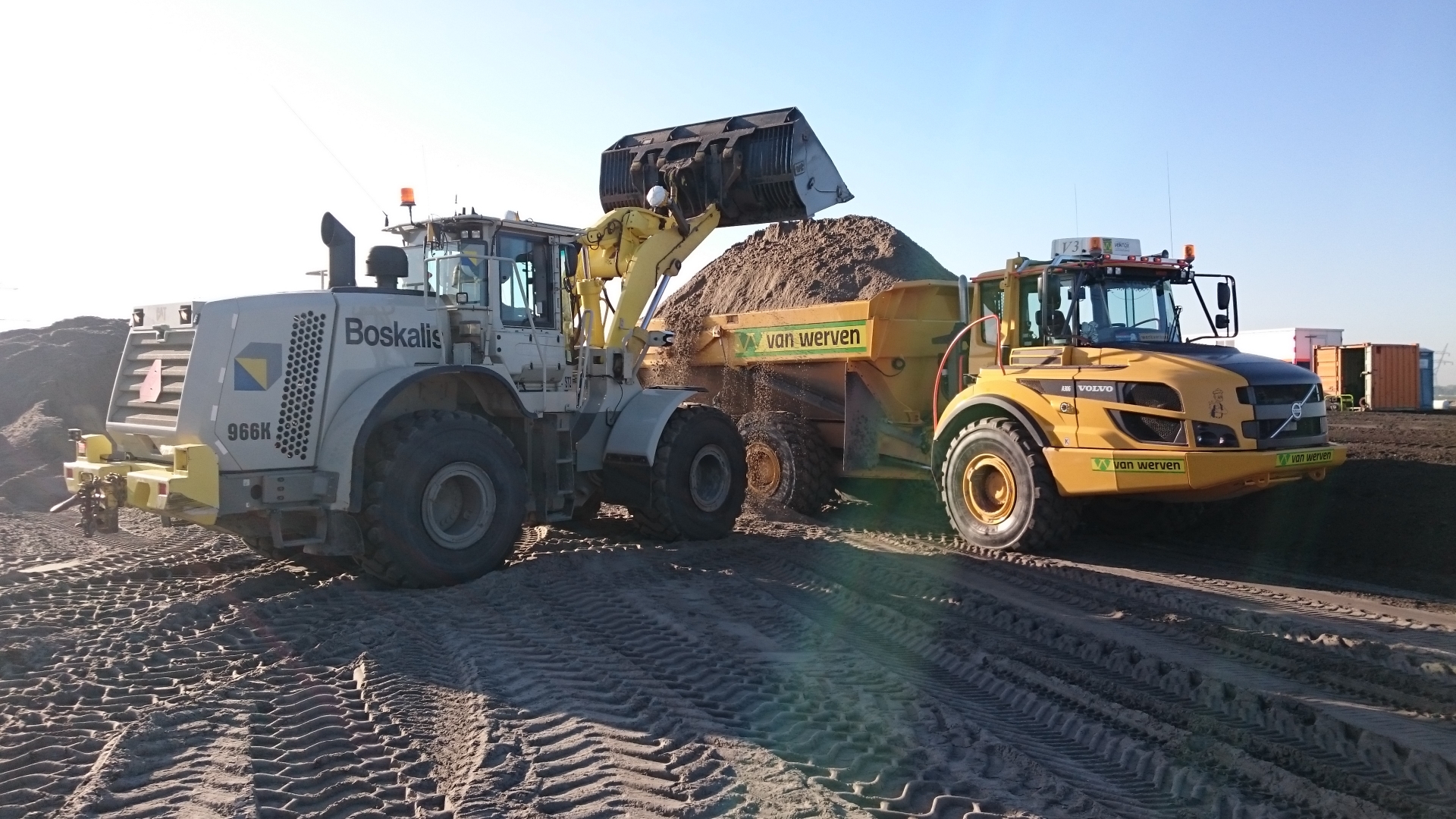 Een witte wiellader van Boskalis stort zand in een gele dumper van Van Werven op het zandlichaam