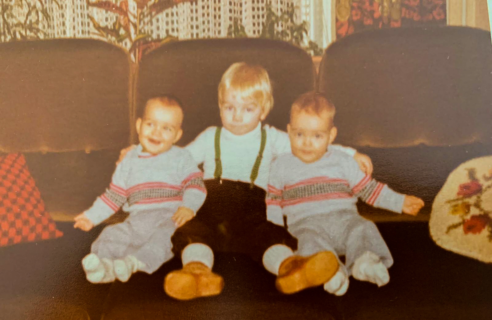 Vergeelde familiefoto: drie kleine jongens naast elkaar op een bank, de middelste met bretels