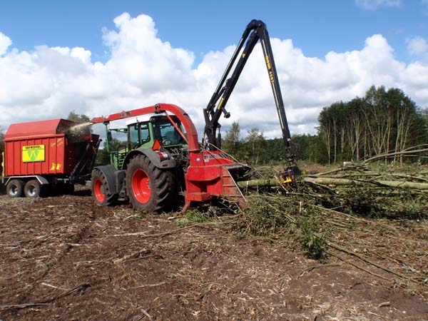 De trekker met versnipperaar en kraantje aan het werk op een bosperceel, met silagewagen