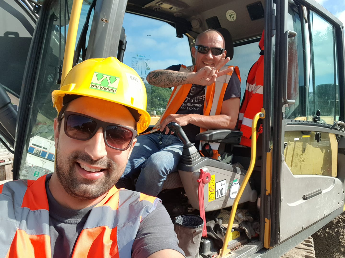 Twee collega’s maken een selfie bij de graafmachine