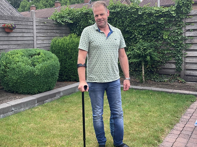 Henk staat met de elleboogkruk op het gazon achter zijn huis