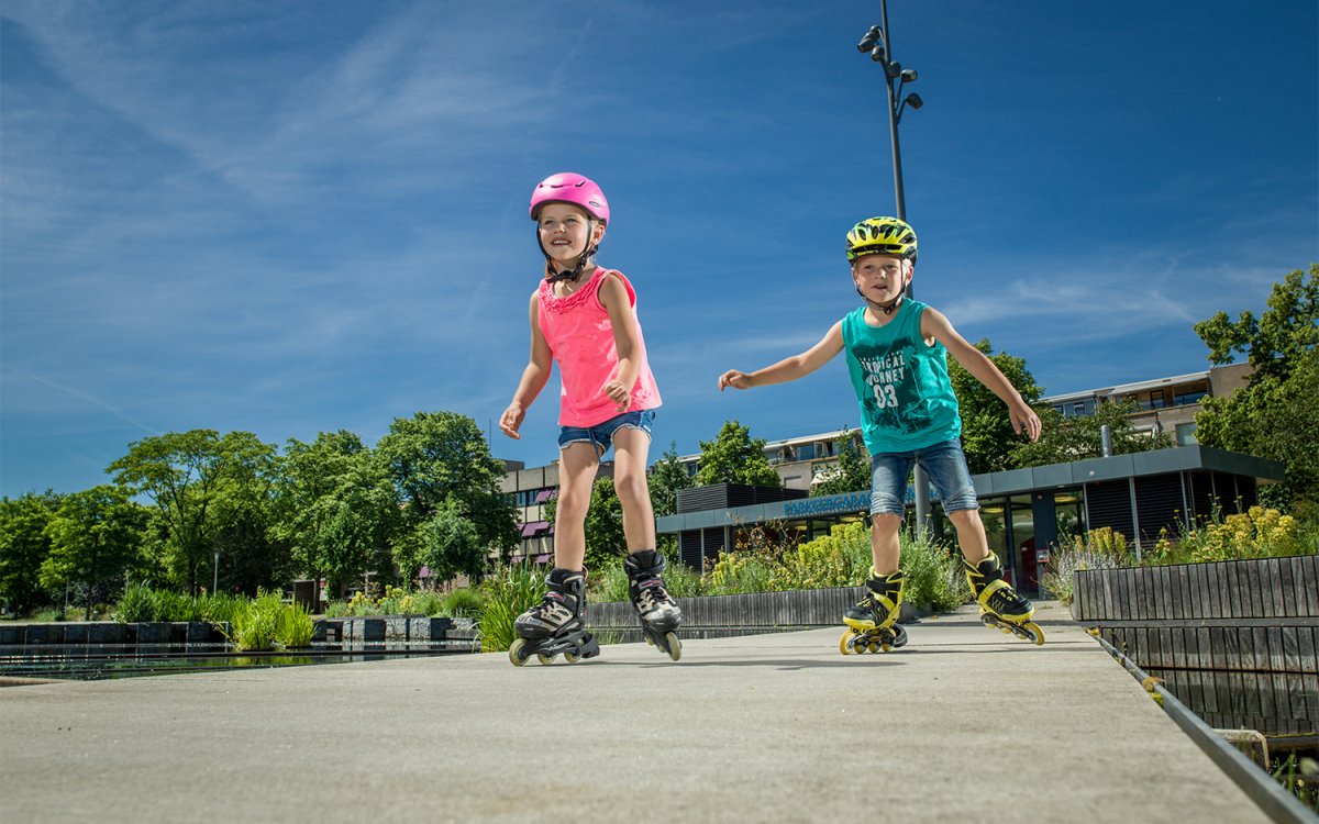 Kinderen skeeleren met stokken over een pad in het groen