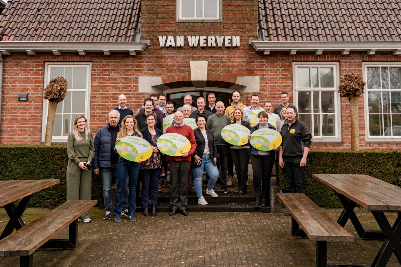 Groepsfoto van vertegenwoordigers van tien goede doelen met ronde borden 'Jullie inzet is onbetaalbaar' voor het Van Werven-kantoor