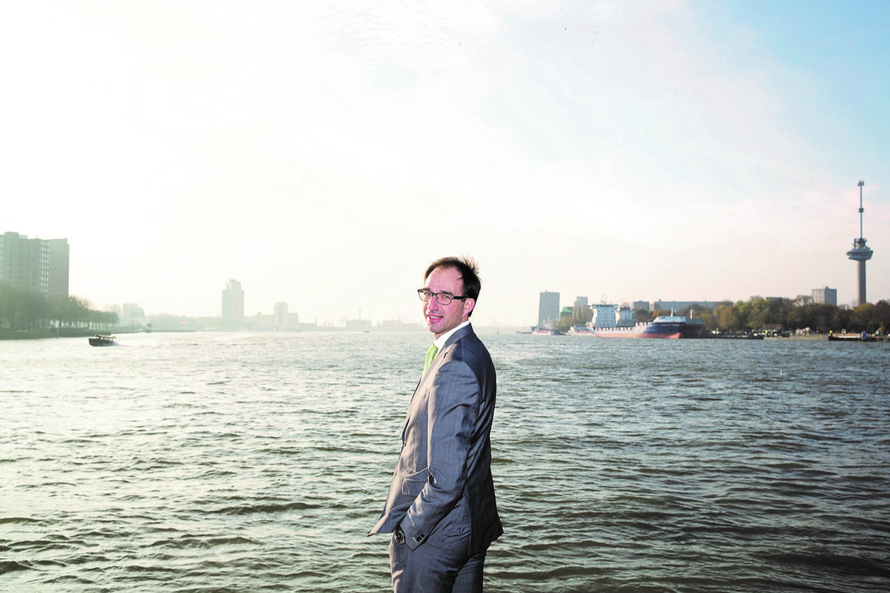 Portret van een man in grijs pak aan het water in Rotterdam, met de Euromast op de achtergrond
