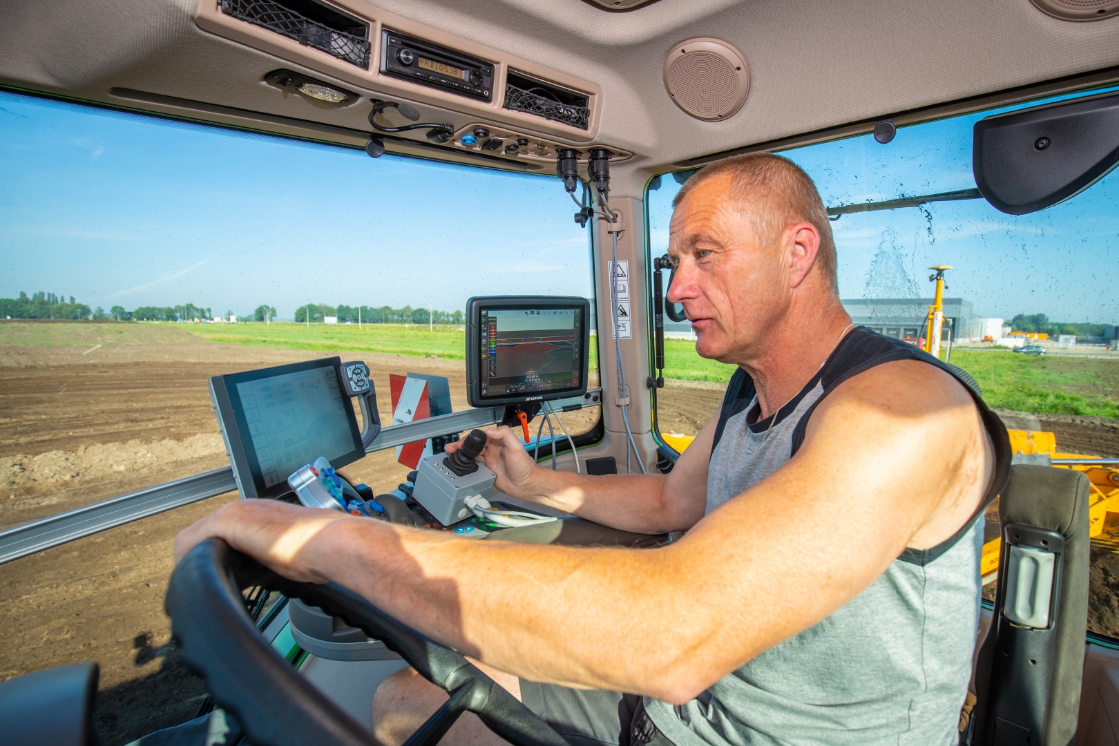 De machinist in de cabine van de Fendt, met de joystick in de hand en de gps-schermen naast het stuur