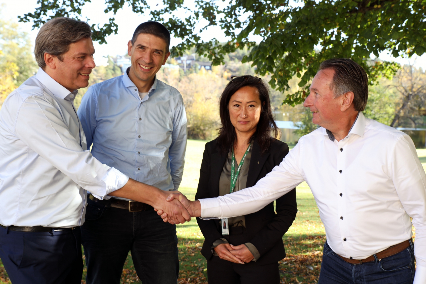 Twee mannen schudden elkaar de hand in een park, met twee collega's naast hen, bij de bekendmaking van de joint venture met Ragn-Sells