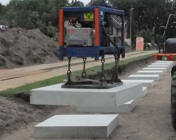De vacuümset aan de kraan tilt een betonplaat; een rij platen ligt klaar langs het spoor