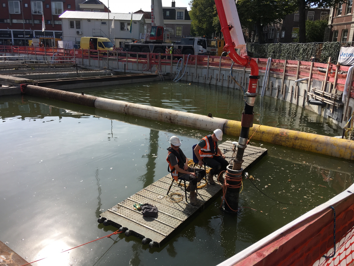 Twee mannen op een drijvend vlot begeleiden de stortbuis van de betonpomp in het water van de bouwkuip
