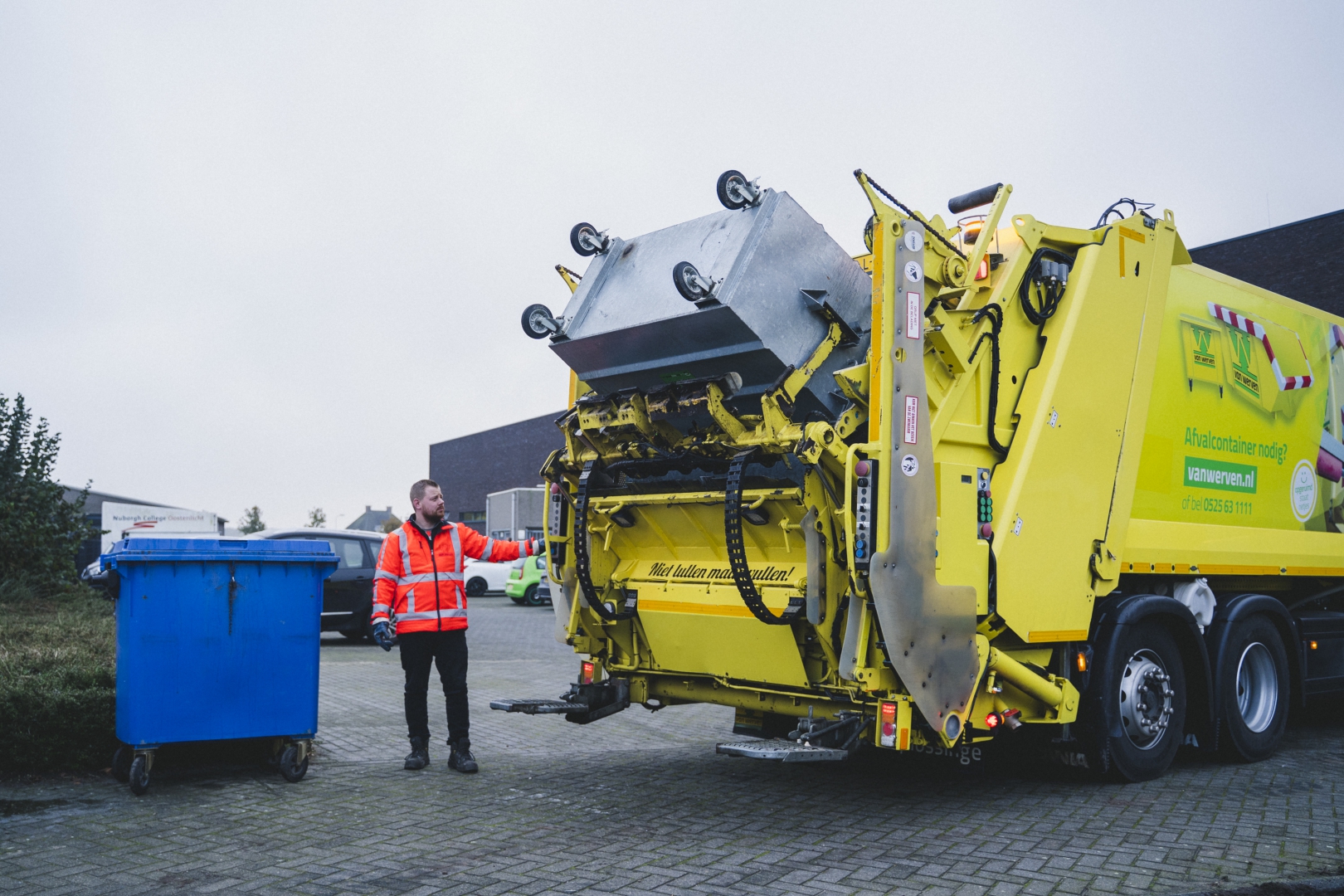 Chauffeur leegt een rolcontainer met de achterlader (kraakperswagen)