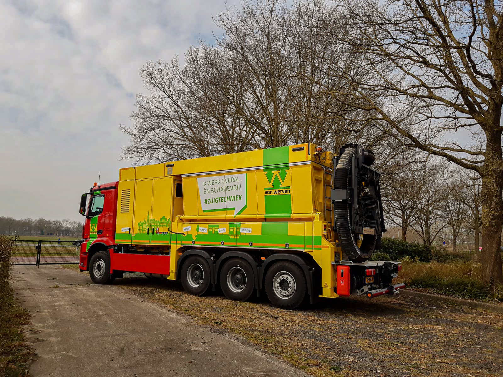 De rood-gele zuigwagen van Van Werven met de tekst 'Ik werk overal én schadevrij! #zuigtechniek' geparkeerd langs een laan met kale bomen