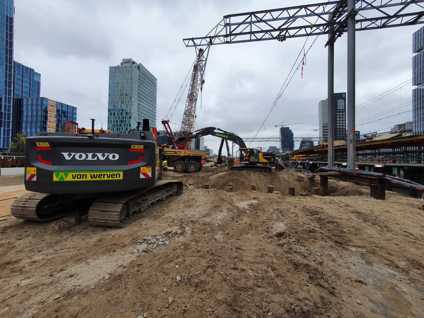 Een Volvo-rupskraan van Van Werven bij de put, met een rode rupskraan van Mammoet en de WTC-toren op de achtergrond
