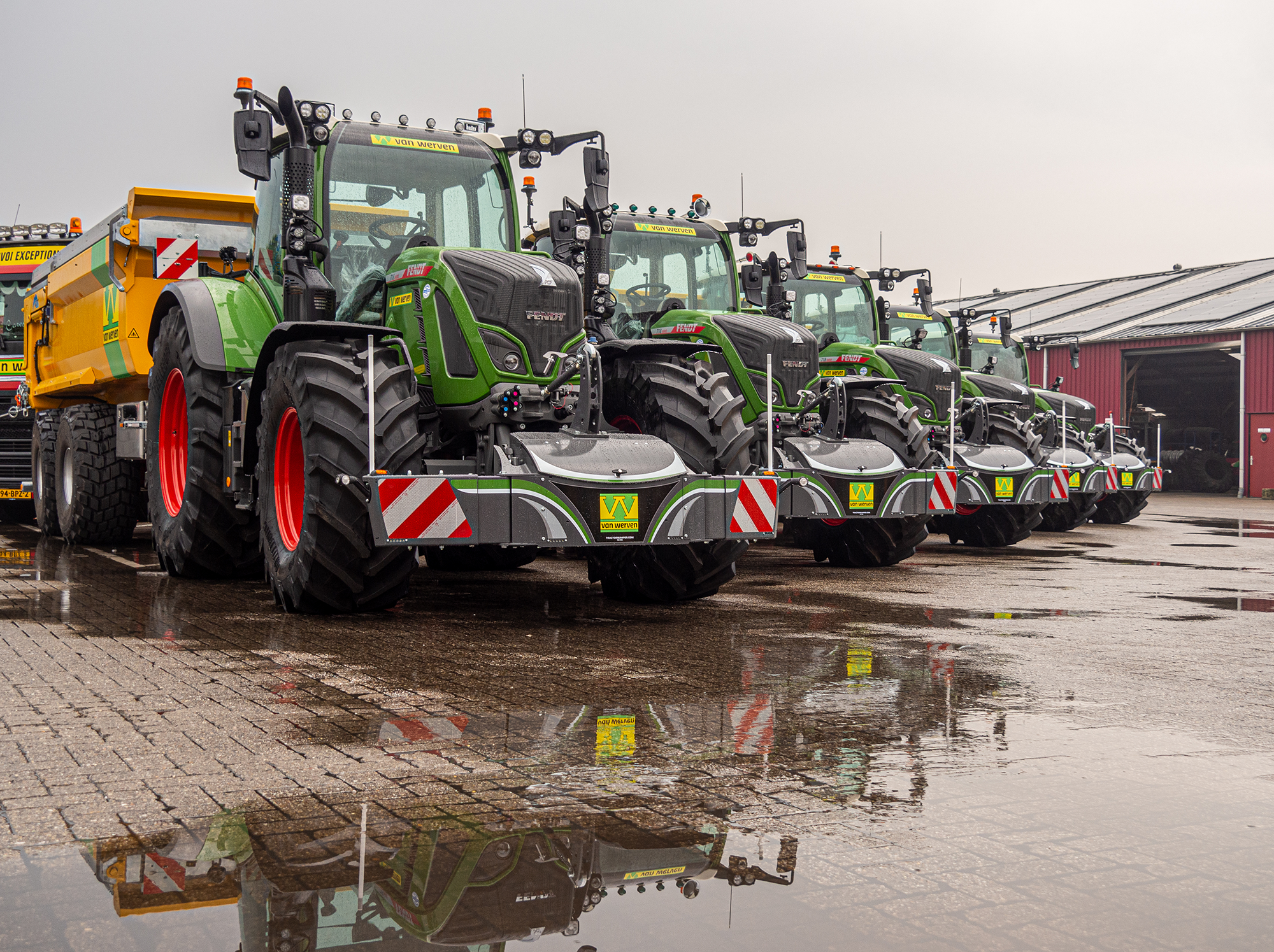 Rij nieuwe Fendt-tractoren met Van Werven-logo naast een gele kipwagen op het natte terrein