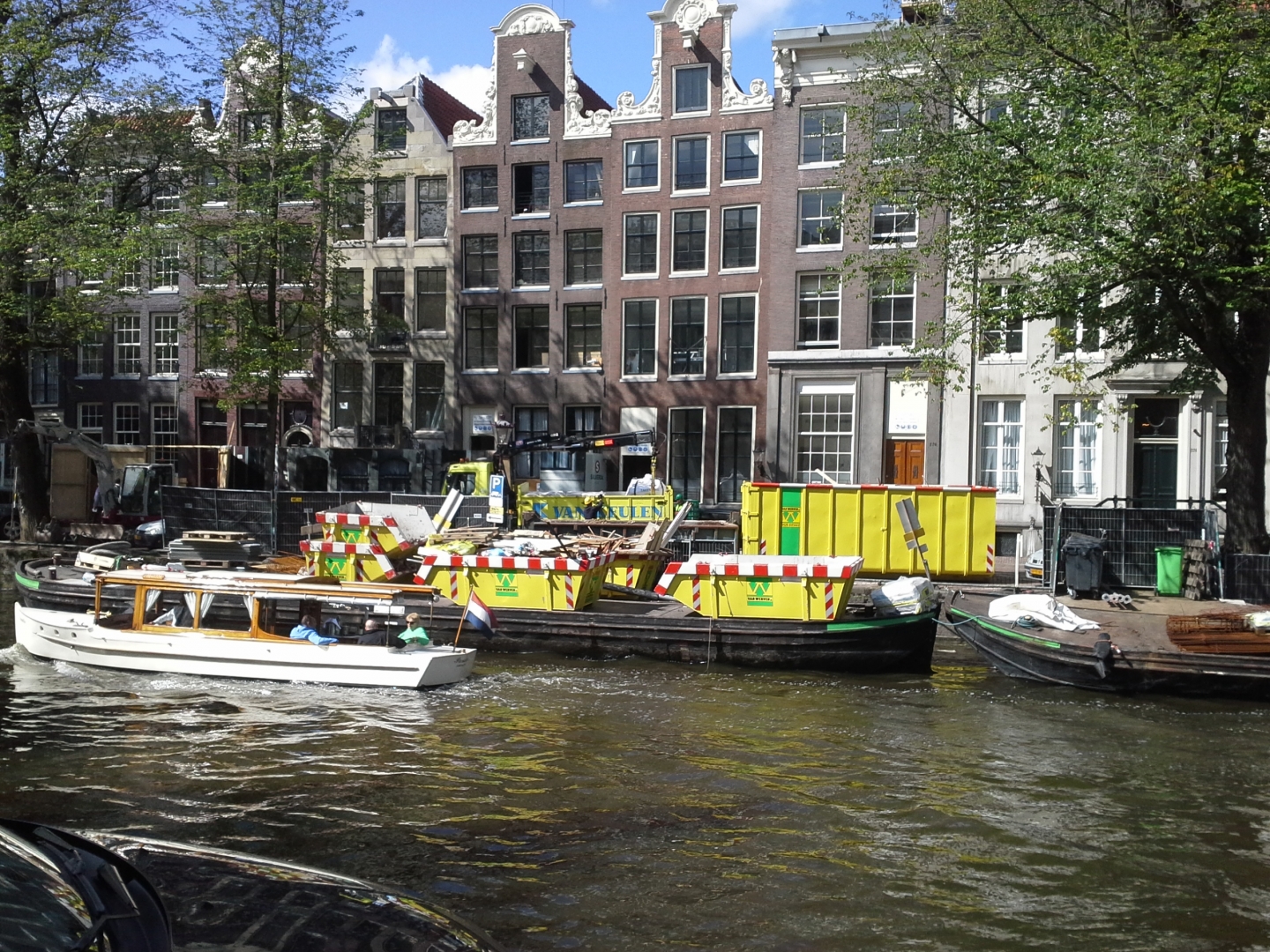 Gele afzetcontainers van Van Werven op een dekschuit in een Amsterdamse gracht, voor de grachtenhuizen van het Pulitzer Hotel
