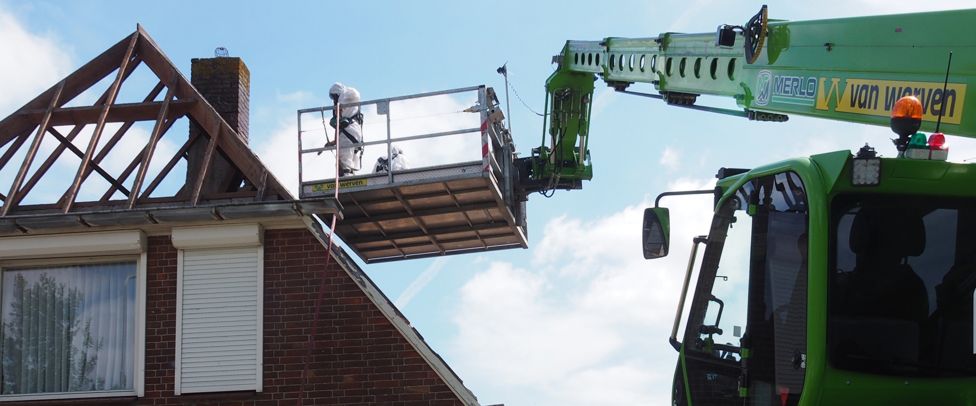 Twee saneerders in witte beschermende pakken werken vanuit een hoogwerkersbak aan een gestript dak