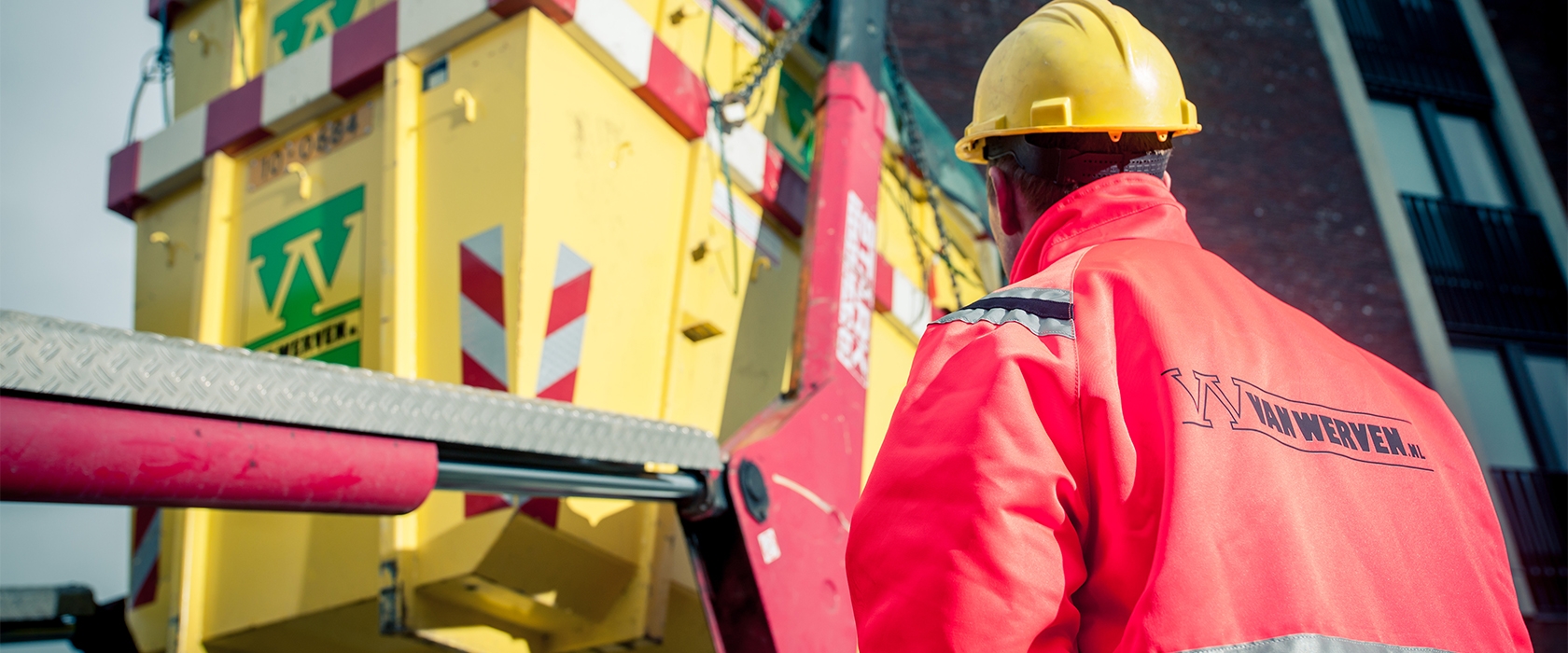 Medewerker met helm bij het laden van een gele afzetcontainer
