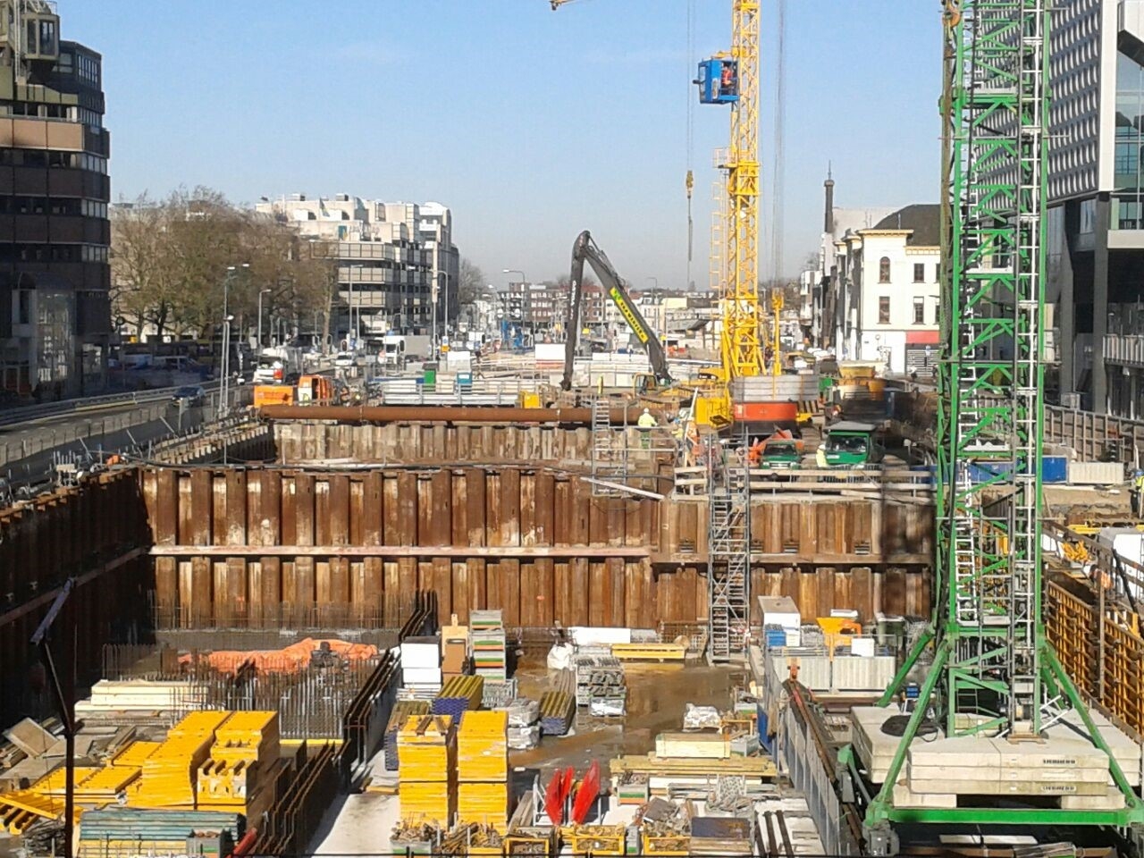 Overzicht van de bouwkuip in de singel, met damwanden, een gele torenkraan en een rupskraan met lange giek
