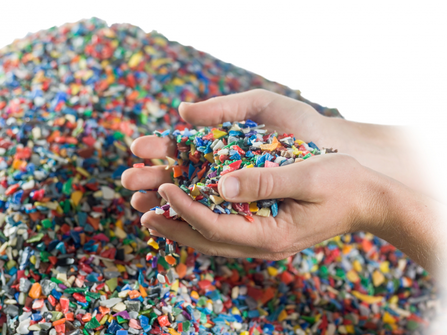 Handen vol kunststof maalgoed boven een berg gekleurde flakes