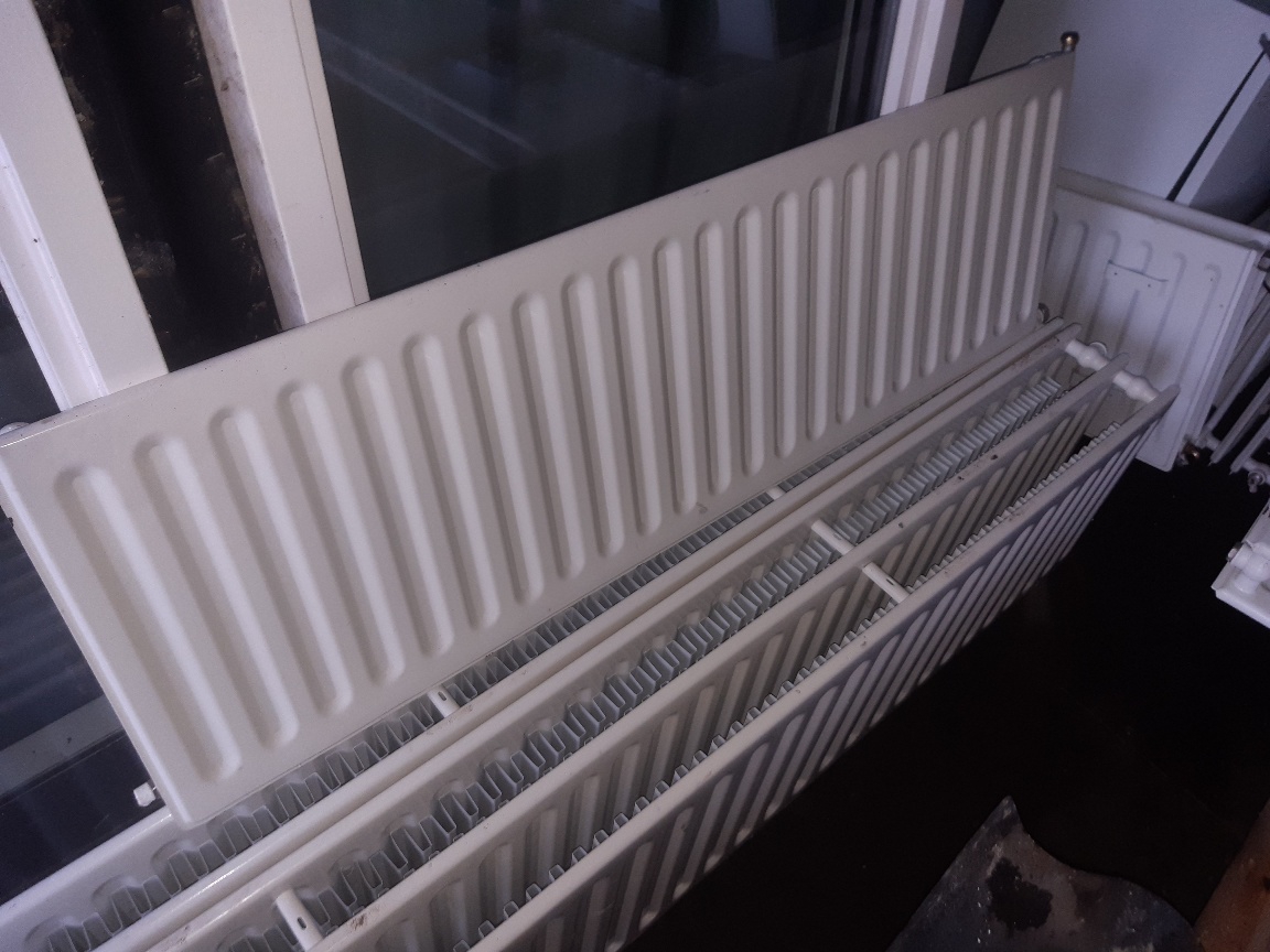 Lange paneelradiator rechtop voor het raam van de opslag, met meer radiatoren ervoor