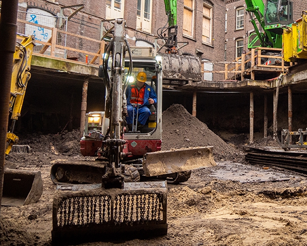 Minikraan graaft onder een Amsterdams pand dat op stalen stempels is onderstut