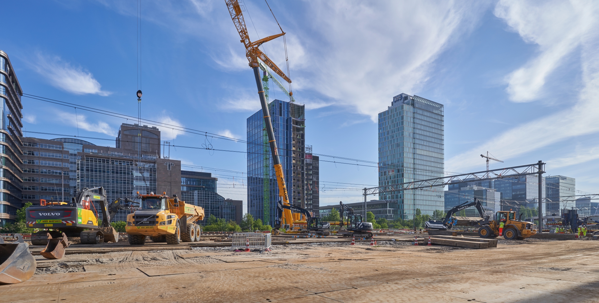 Panorama van het spoorwerkterrein op de Zuidas: kranen en een dumper van Van Werven tussen de bovenleidingportalen, met de telekraan en de WTC-toren erachter