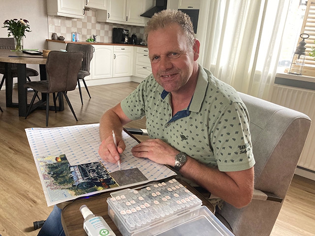 Henk werkt aan de keukentafel aan een diamond painting, de bakjes met steentjes voor zich