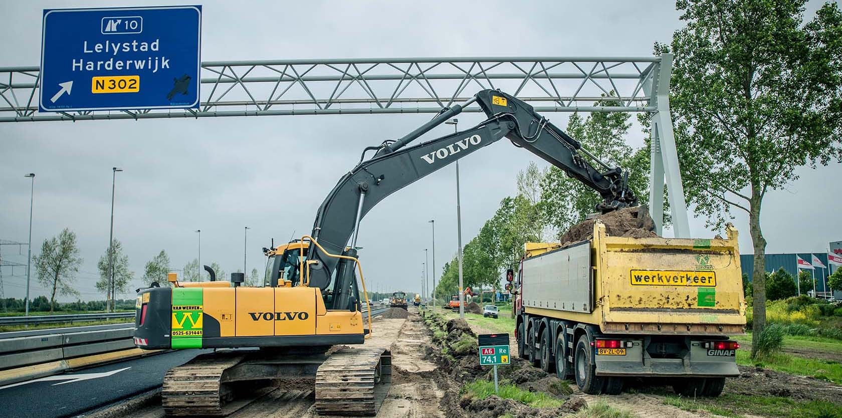 Een Volvo-rupskraan van Van Werven laadt een kipper met grond langs de A6, onder het portaal met het bord naar de N302
