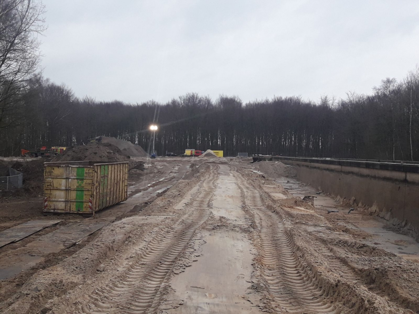 De betonnen goot vanaf de kopse kant gezien, met diepe rupssporen in de modder en een container langs de kant