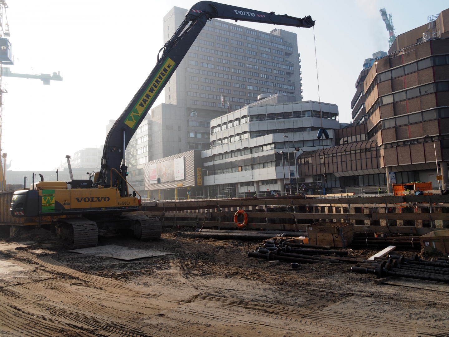 De Volvo-rupskraan met lange giek van Van Werven aan de rand van de bouwkuip, in de ochtendnevel voor de kantoorgebouwen