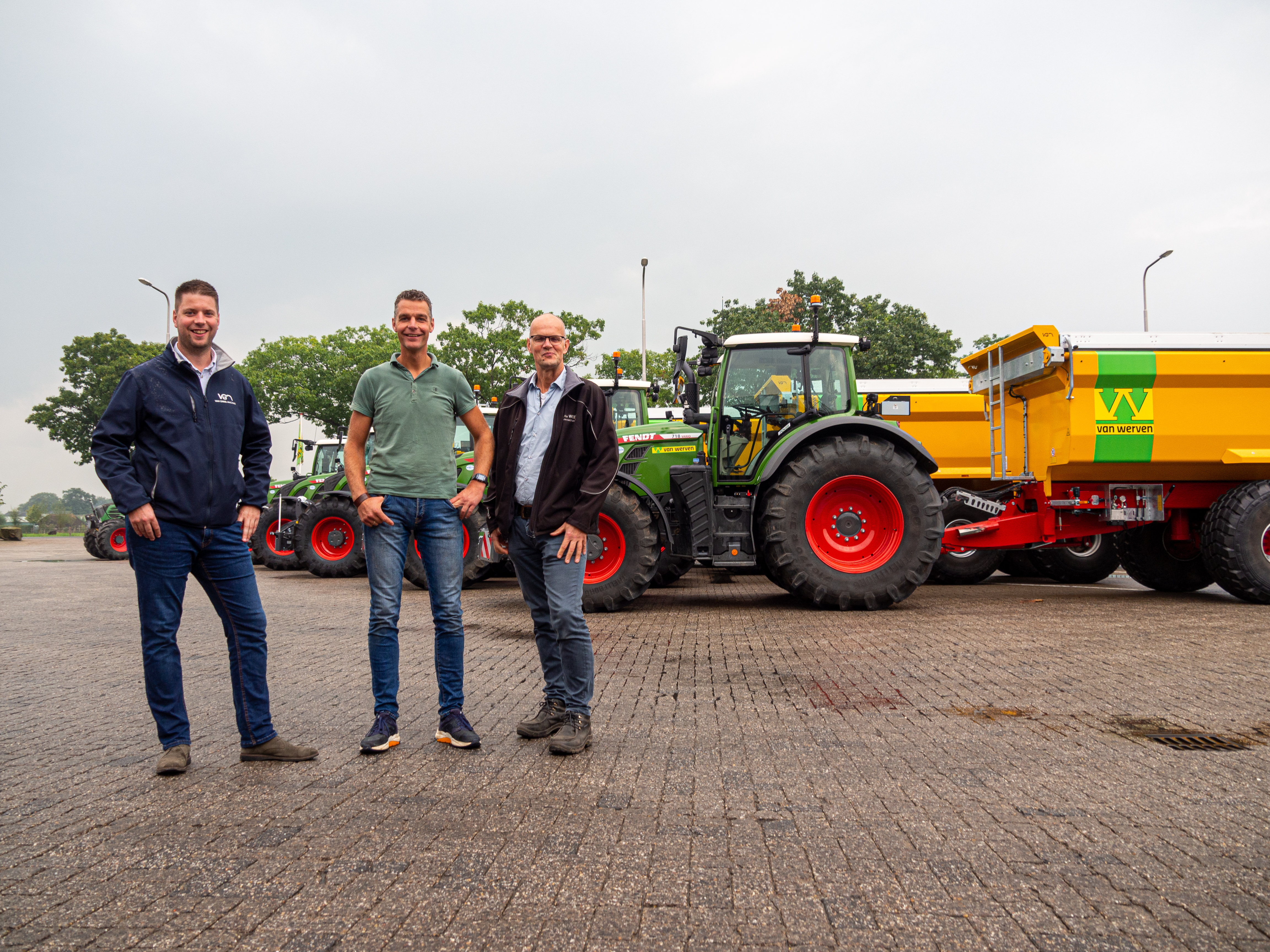 Drie mannen poseren voor een Fendt-tractor met gele kipwagen