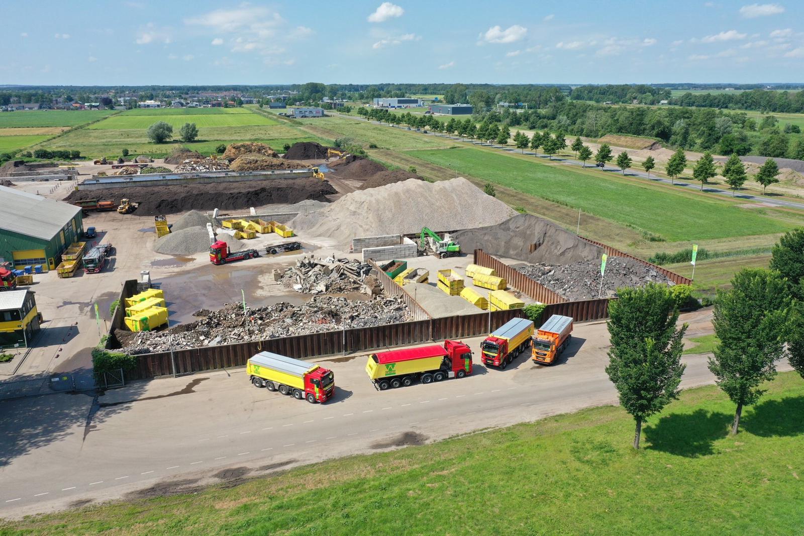 Luchtfoto van Recycling Hattemerbroek met puin- en grondbergen, gele containers en vier vrachtwagens langs de Middeldijk