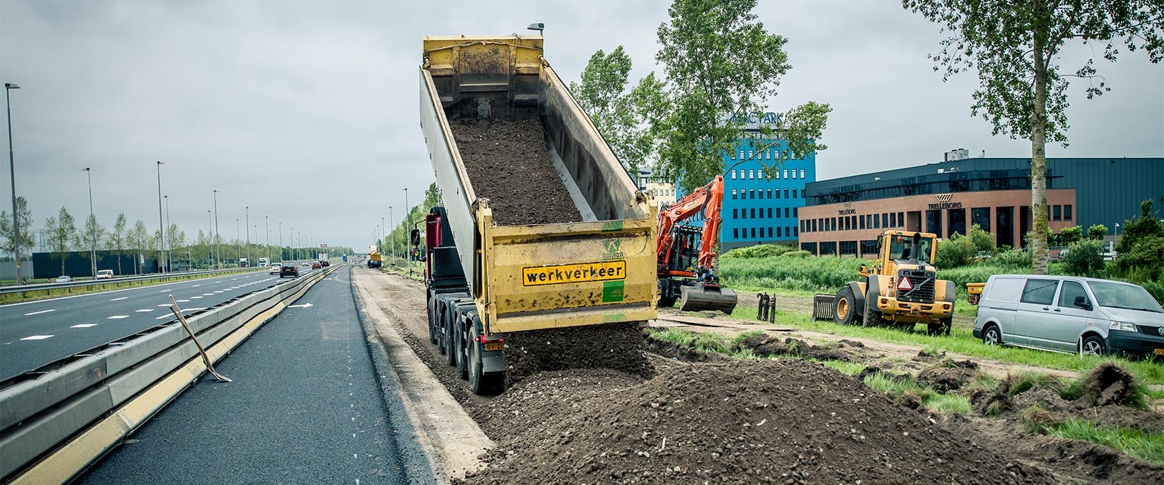 Een kiepauto met het opschrift "werkverkeer" stort menggranulaat naast het bestaande asfalt