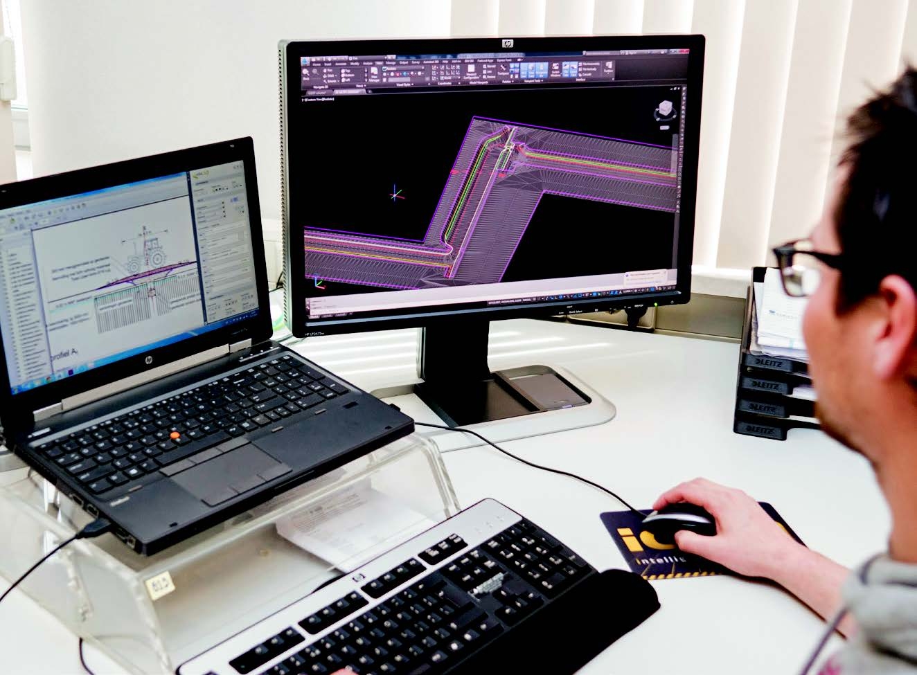 Een werkvoorbereider werkt op kantoor aan twee schermen met het 3D-terreinmodel en het dwarsprofiel van een project