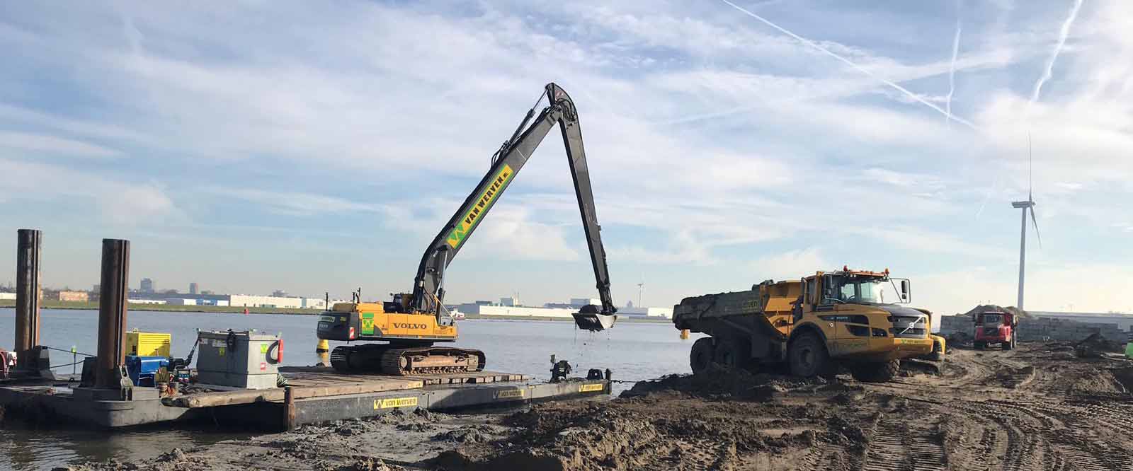 Een Volvo-kraan met lange giek baggert vanaf het Van Werven-ponton, terwijl een dumper op de kant wacht; rechts draait een windmolen