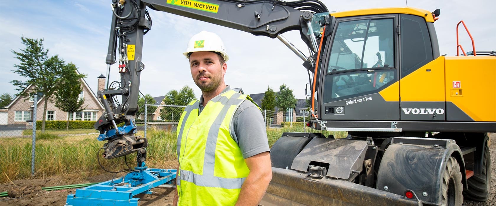 De machinist staat in geel hesje en met witte helm voor zijn Volvo-mobiele kraan met hydraulisch aanbouwdeel