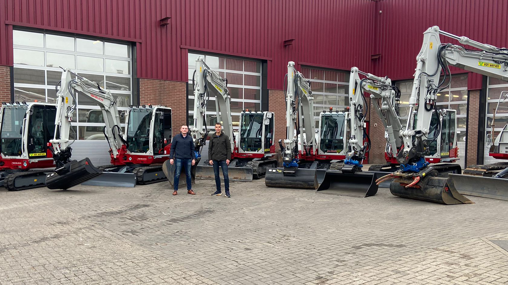 Zes nieuwe Takeuchi-kranen op een rij voor de rode loods, met twee mannen ertussen