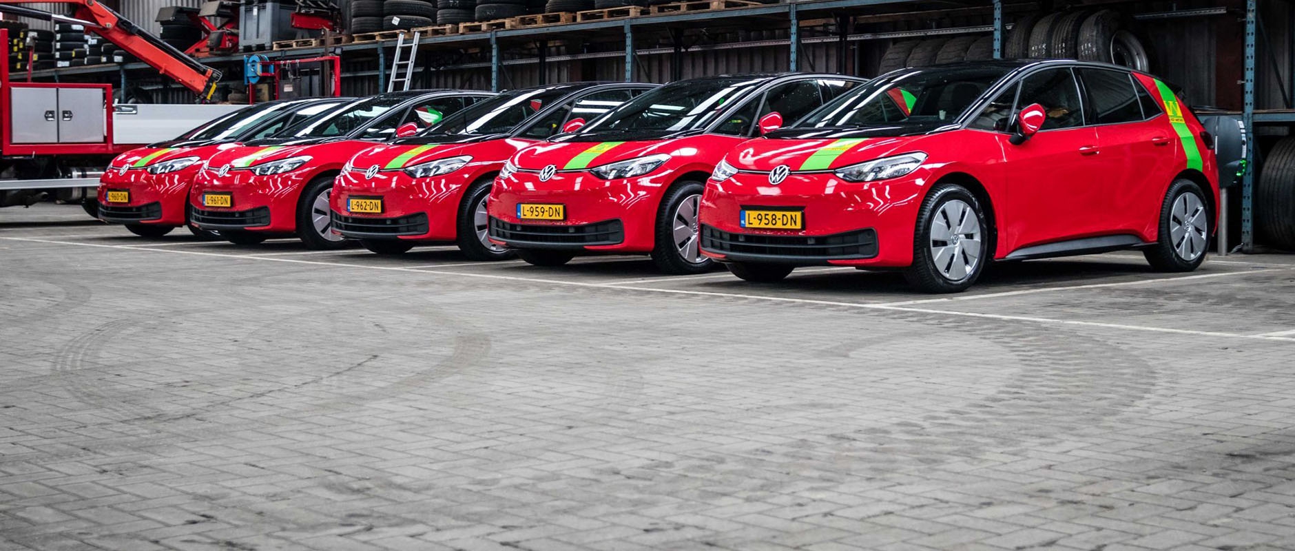 Vijf rode elektrische Volkswagen ID.3's met groene Van Werven-striping staan op een rij in de loods