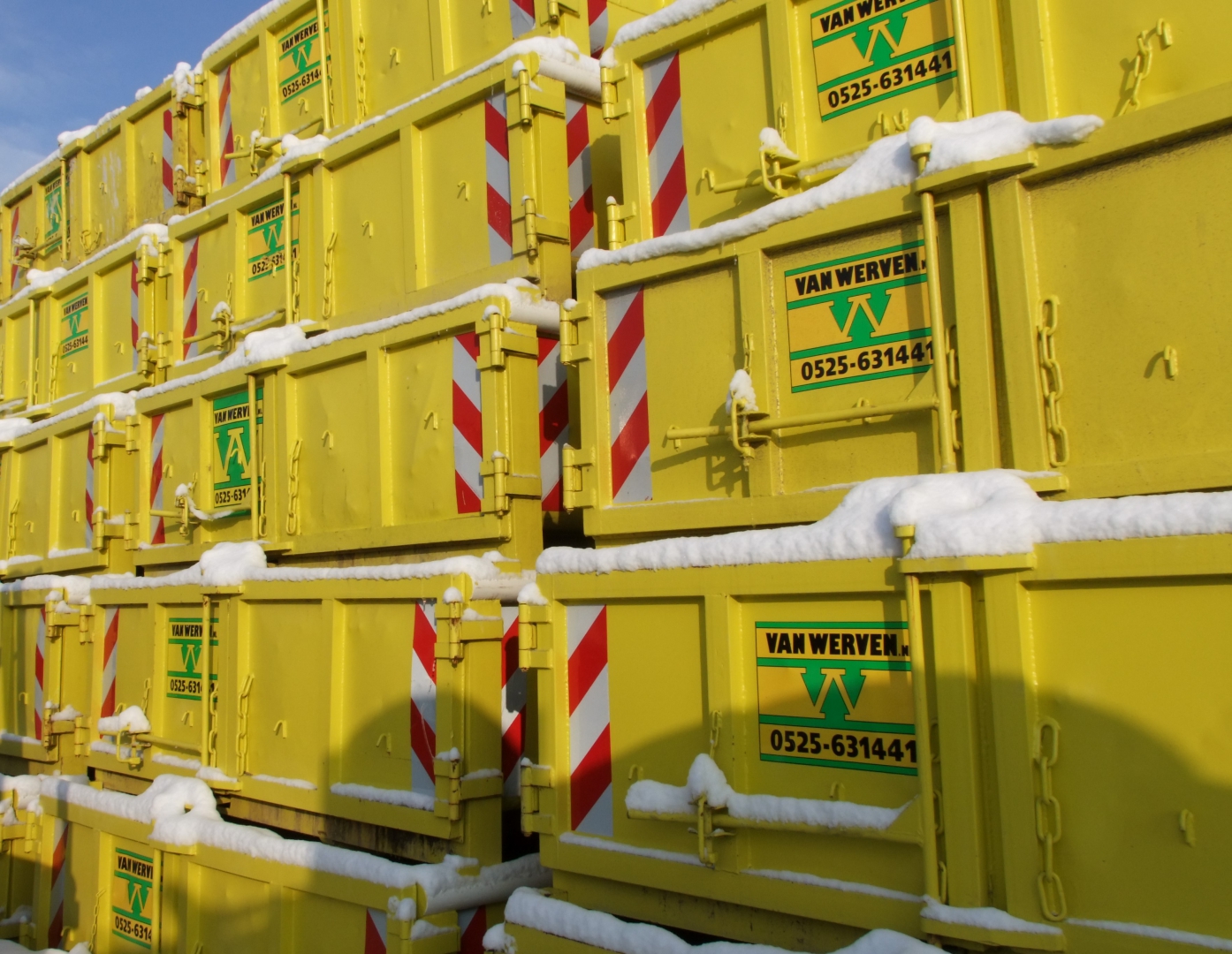 Gestapelde gele Van Werven-containers met een laagje sneeuw