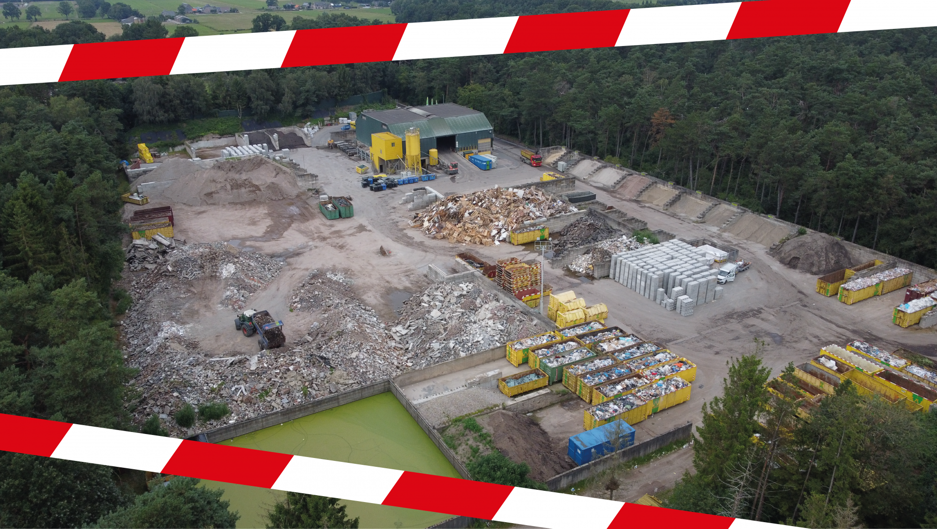 Luchtfoto van Recycling Oldebroek met puinbergen, gele containers en de groene loods, omkaderd door rood-wit afzetlint