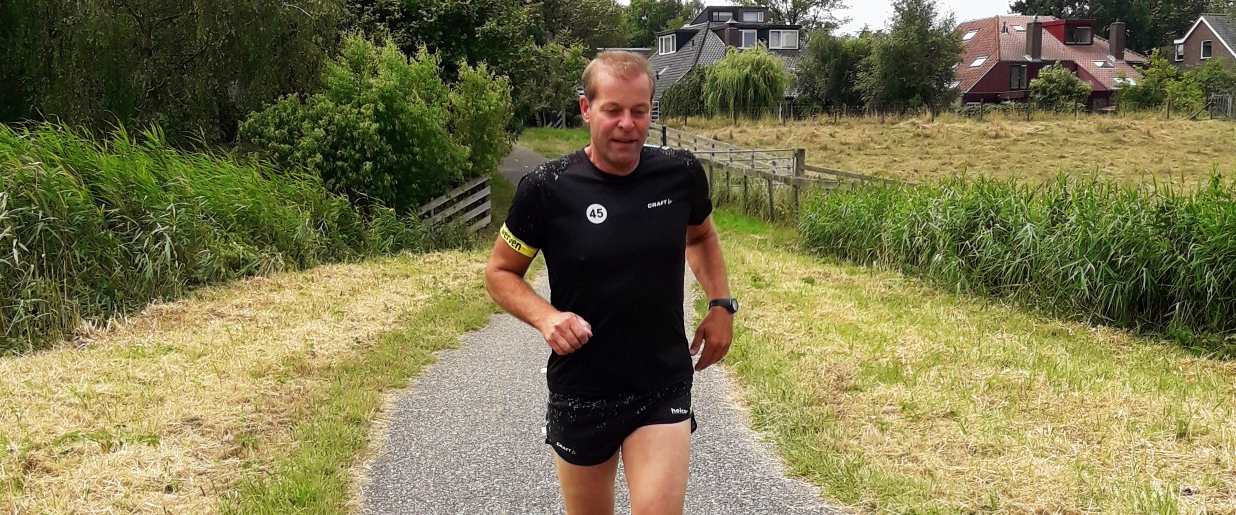 Een hardloper in het zwarte Van Werven-runningshirt op een landweg, met de gele armband om de bovenarm