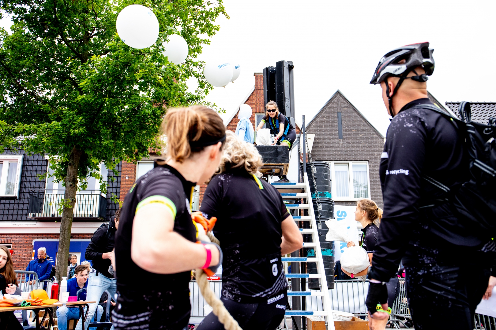 Deelnemers met touwen en zandzakken bij de trap-hindernis, met witte ballonnen boven het parcours