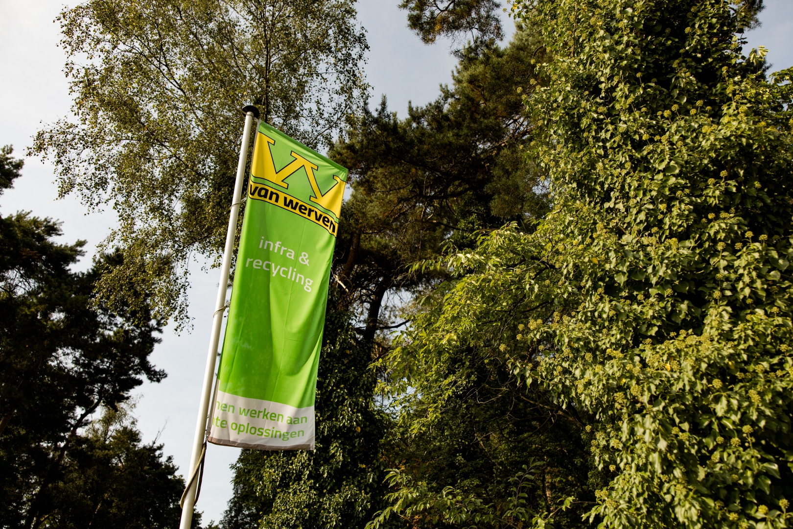 Groene Van Werven-vlag met de tekst 'infra & recycling' wappert tussen de bomen