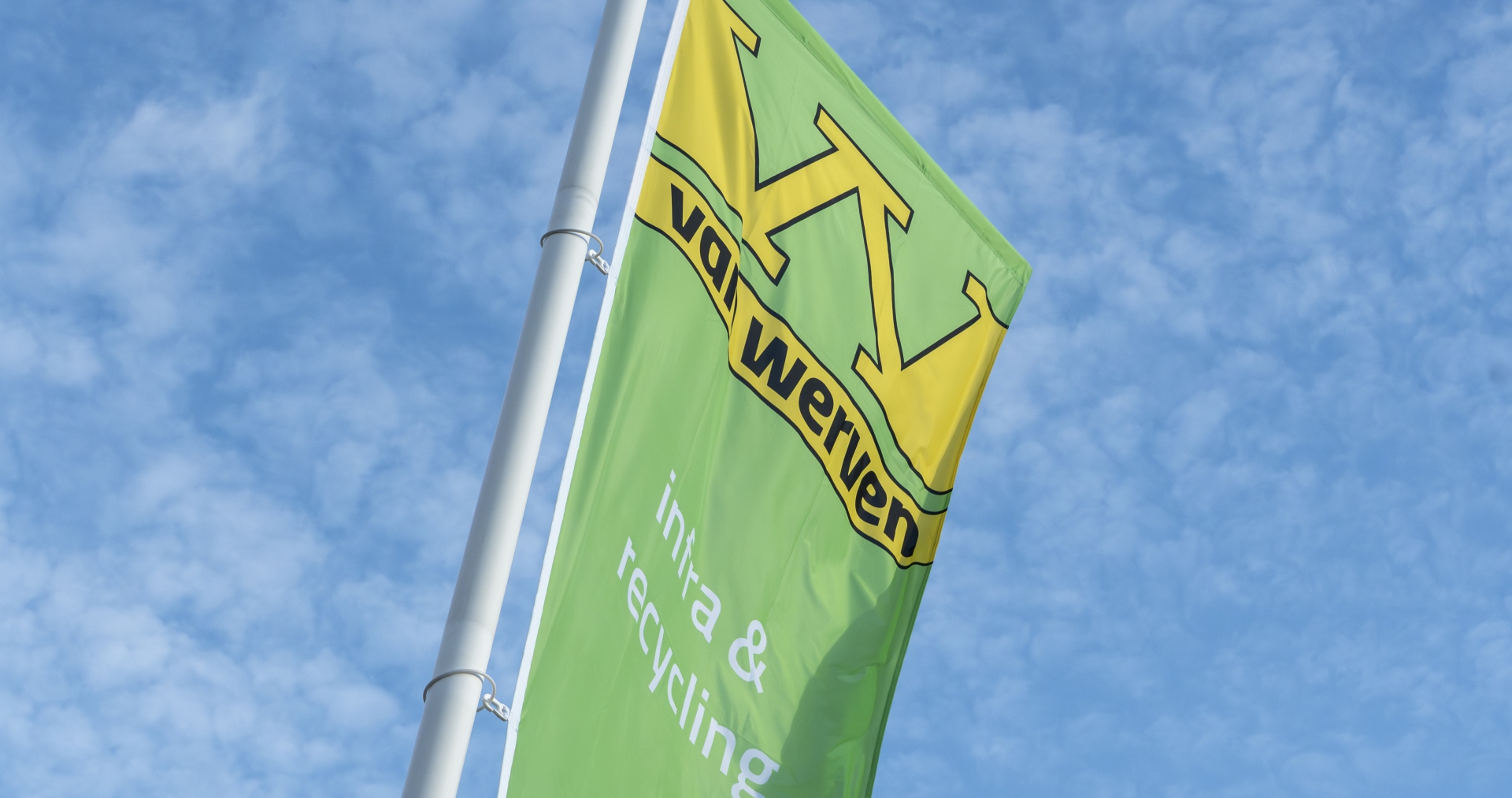 Groene Van Werven-vlag met de tekst 'infra & recycling' tegen een blauwe lucht met wolken