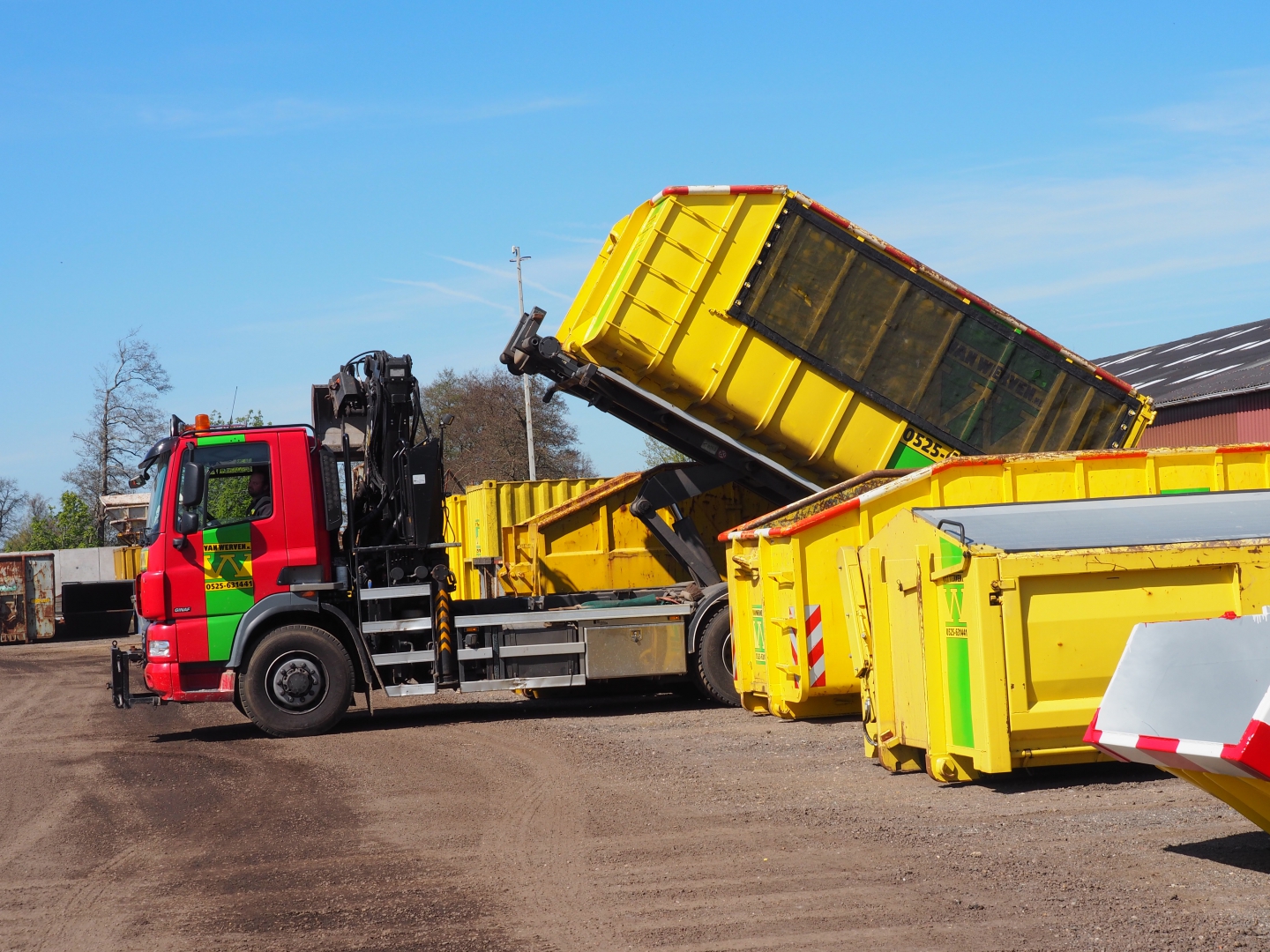 Containerauto zet een gele afzetcontainer neer op het terrein in Oldebroek