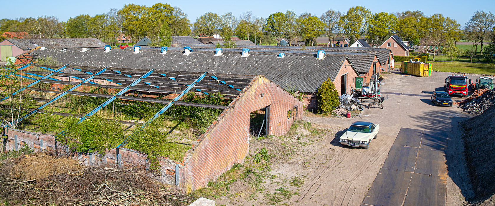 Vier lange kippenschuren met asbestdaken op een erf, deels al gestript tot het stalen spant, met een oldtimer op het voorterrein