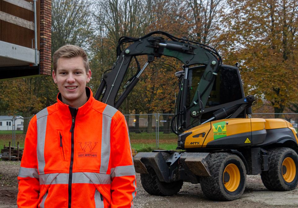 De jonge medewerker in oranje werkjas voor een Van Werven-graafmachine op de bouwplaats