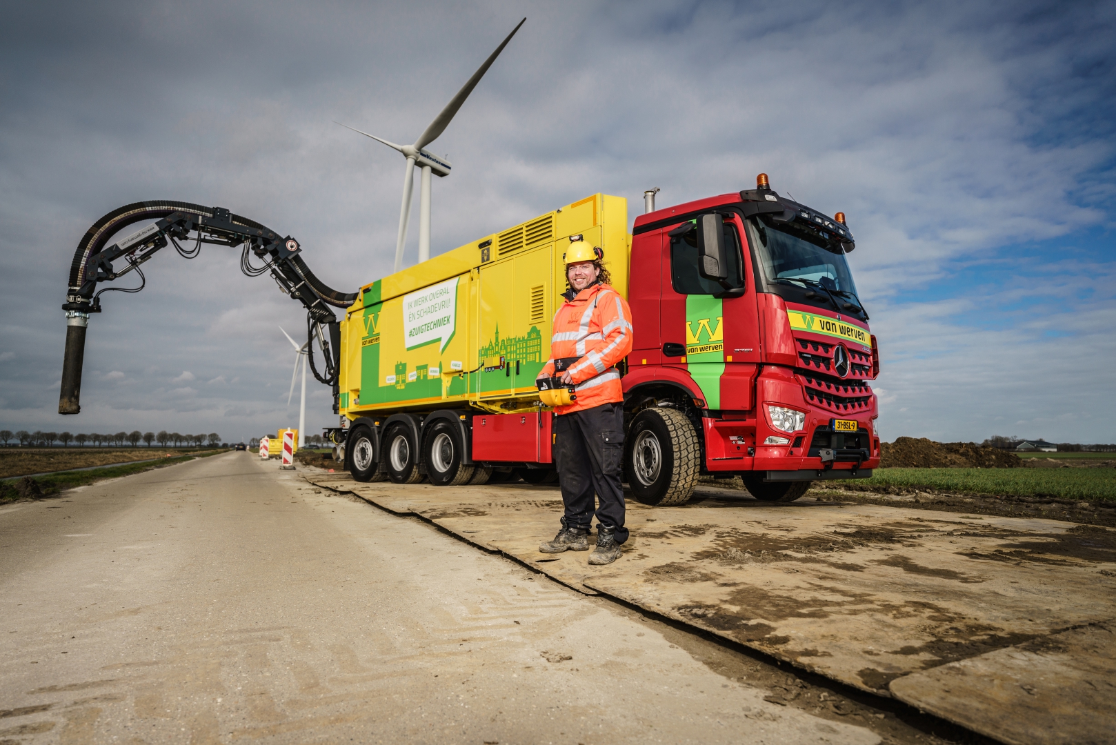 Machinist bedient de grondzuigwagen met de afstandsbediening, met windmolens op de achtergrond